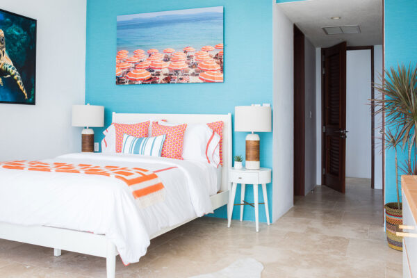 Vibrant Blue Queen Suite at Champagne Shores Villa, featuring a bright blue accent wall, a white bed with colorful pillows and an orange throw blanket, and modern bedside tables with lamps.