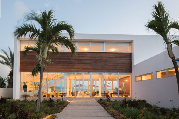 Exterior view of Champagne Shores Villa at dusk, featuring modern architecture, large windows, and a beautifully landscaped garden with palm trees.