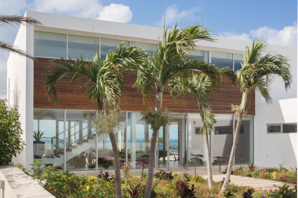 Exterior view of Champagne Shores Villa, featuring modern architecture, large windows, and a beautifully landscaped garden with palm trees.