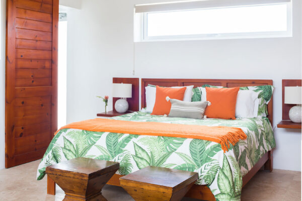 King Garden Suite at Champagne Shores Villa, featuring a king-size bed with green and white leaf-patterned bedding, orange accents, and wooden bedside tables. The room has large wooden sliding doors and a small window providing natural light.