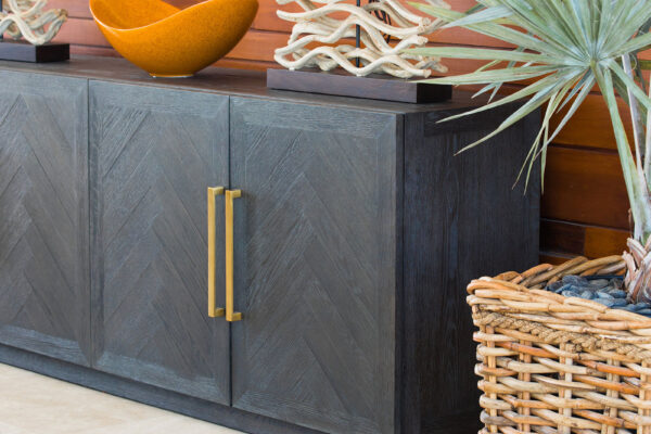 Decorative sideboard at Champagne Shores Villa, featuring a dark wood chevron-patterned cabinet with gold handles. On top are two unique driftwood lamps with white shades, an orange bowl, and a tropical plant in a woven basket.