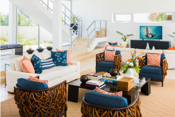 Elegant and spacious living area at Champagne Shores Villa in Anguilla, featuring comfortable seating with blue and orange cushions, a coffee table with books, and a staircase leading to the upper floor.