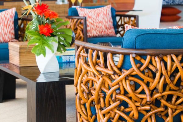 Close-up of a living area at Champagne Shores Villa, featuring a woven rattan chair with blue cushions, a black coffee table with a vase of vibrant flowers, and a background of wooden wall panels and tropical decor.