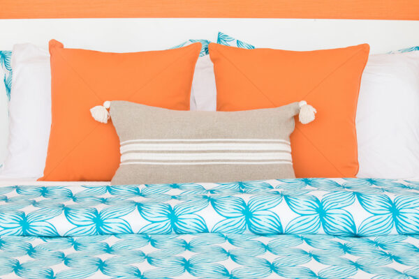 Close-up of orange queen suite bed at Champagne Shores Villa, featuring vibrant orange pillows, a beige decorative cushion, and a blue and white leaf-patterned duvet.