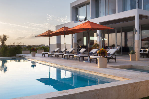 Luxurious poolside area at Champagne Shores Villa in Anguilla with sun loungers under orange umbrellas, adjacent to the modern villa and overlooking serene landscapes.