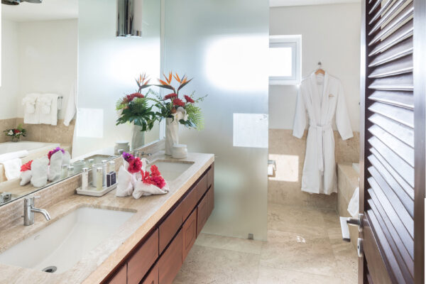 Primary Suite Ensuite at Champagne Shores Villa, featuring a double vanity with a spacious countertop, wooden cabinets, and a large mirror. The ensuite includes a separate bathtub, and a shower area.