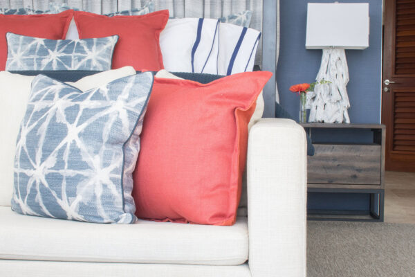 Close-up of the primary suite at Champagne Shores Villa, featuring a cozy seating area with blue and white patterned pillows, red accents, and a wooden nightstand with a decorative lamp and flower vase.