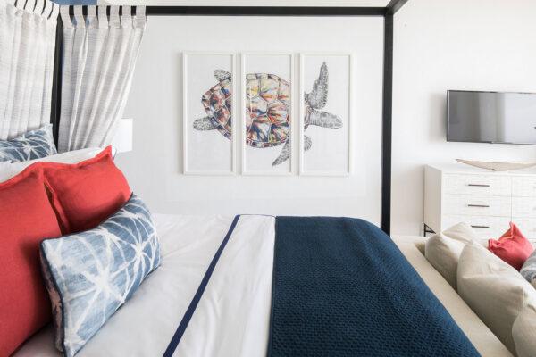 Primary suite at Champagne Shores Villa featuring a four-poster bed with red and blue pillows, nautical-themed decor, and a large framed turtle artwork on the wall.