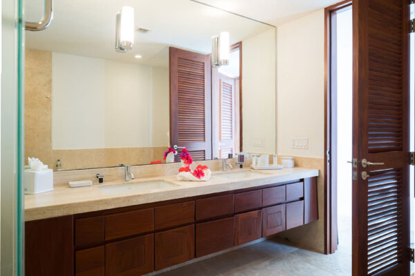 Ensuite bathroom in the primary suite at Champagne Shores Villa, featuring a large mirror, dual sinks, and a spacious countertop. The bathroom has wooden cabinetry and a glass shower door.