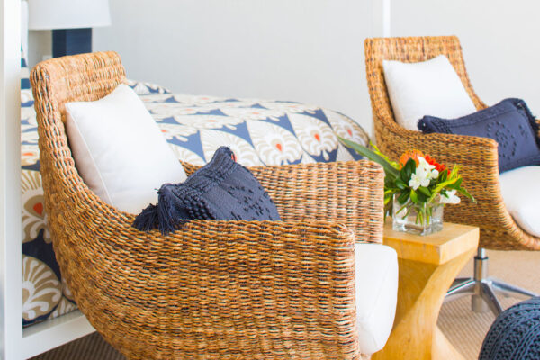 Close-up of wicker chairs with cushions in the secondary primary suite at Champagne Shores Villa, with a patterned bed, side table, and modern artwork in the background.