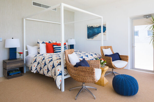 Interior of the secondary primary suite at Champagne Shores Villa, featuring a four-poster bed with patterned bedding, wicker chairs with cushions, a cozy blue pouf, and modern decor.